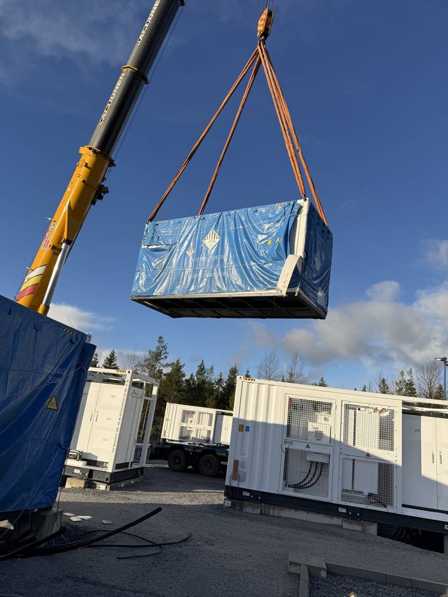 Batterikontainer heises med mobilkran, BESS-containere i bakgrunnen
